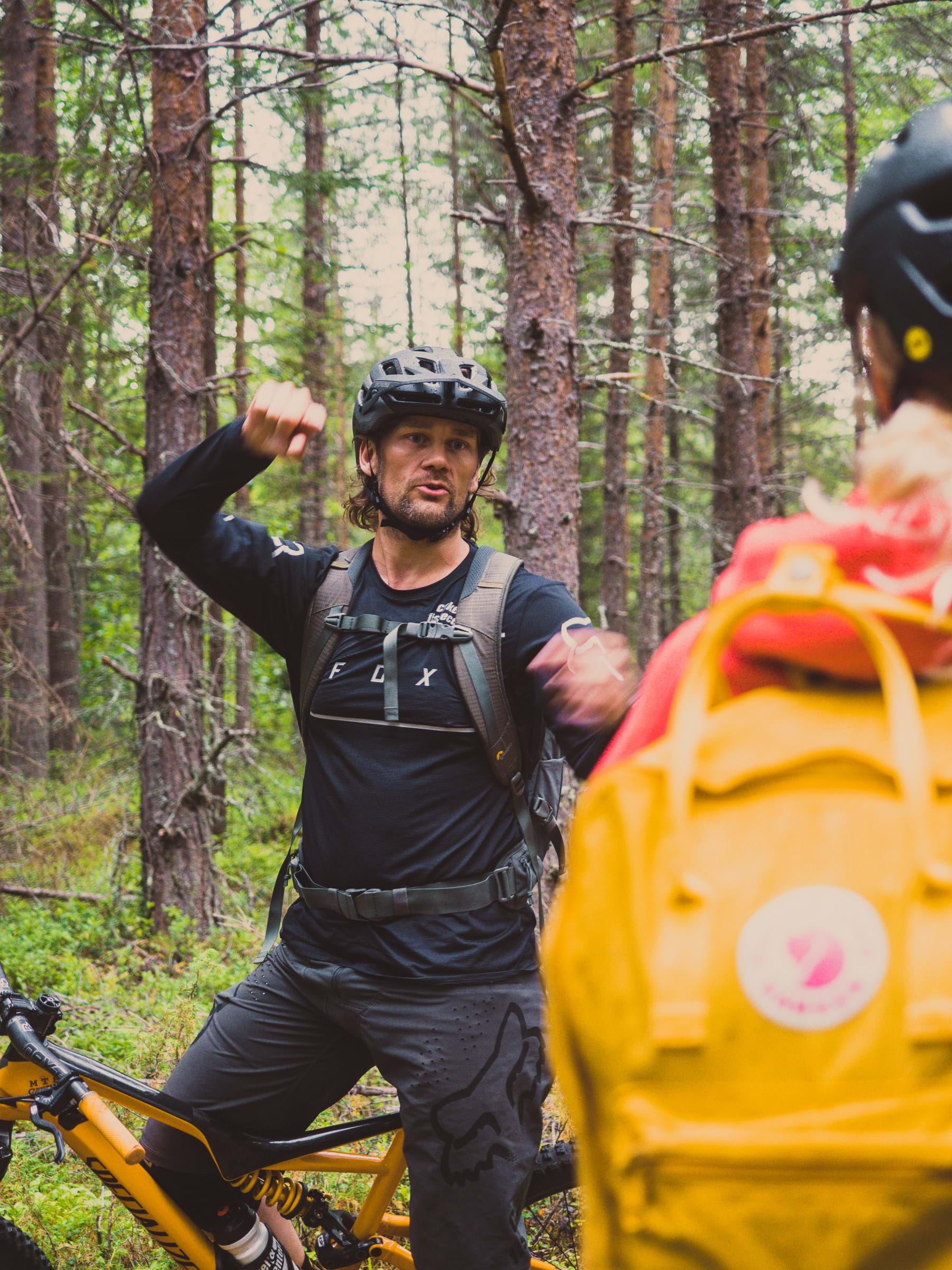 Standing in the woods, Robert is leaning against his bicycle and gesturing with great empathy.