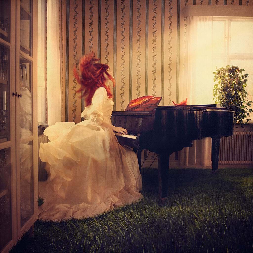 LisaLove is sitting at a piano wearing a sweeping dress in a room with a mansion feel, but where the floor should be, there is a lawn instead.