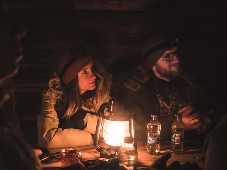 En man och en kvinna sitter framför en tänd lykta i mörkret och lyssnar uppmärksamt till en tredje person utanför bild