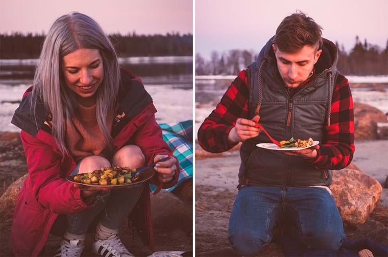 Agnes and Konrad sits on a rock and eats food cooked outdoors