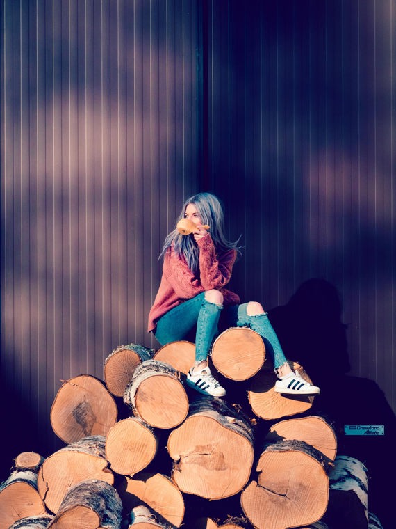 Agnes sits on a pile of logs and drinks from a cup.