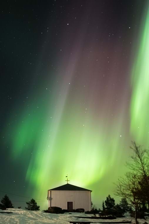 Bjuröklubbs Chapel with a magnificent aurora borealis in the background that covers almost the entire starry sky.