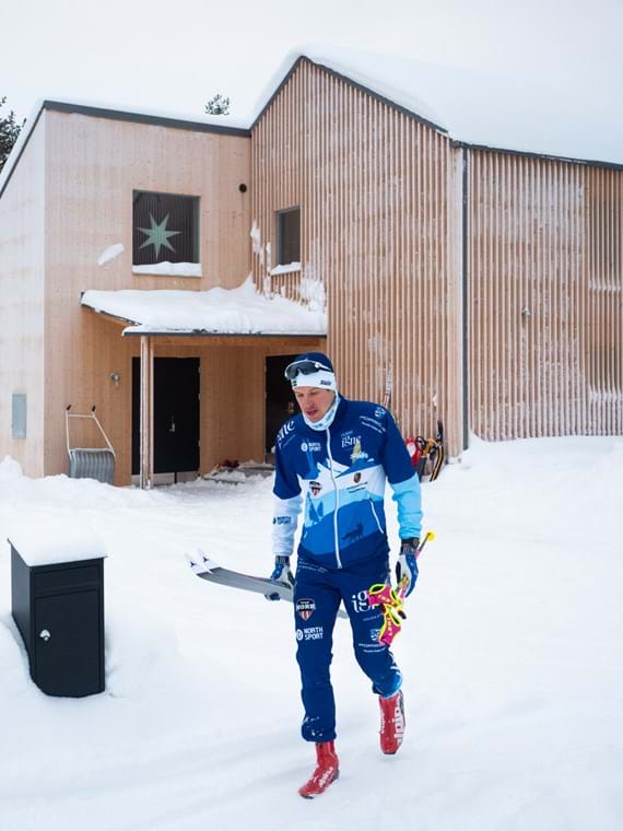Klas stands outside his house with the cross-country skis in one hand and the poles in the other.