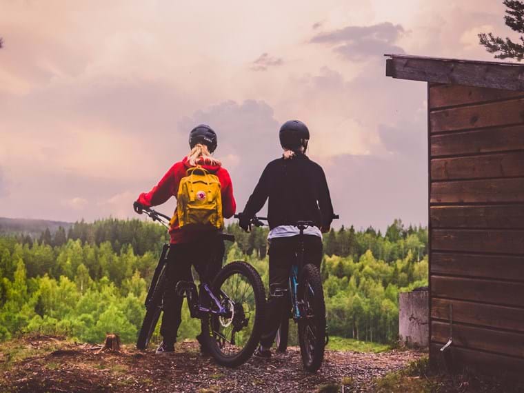 Hanna Fjellsteft och Jeanette står med cyklarna uppe på en kulle och njuter av utsikten.