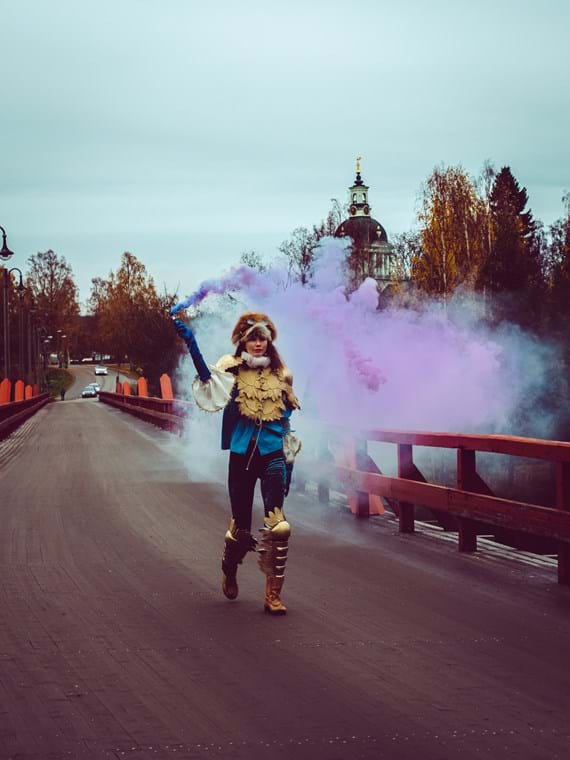 LisaLove Bäckman går över Lejonströmsbron iklädd en dramatisk kostym och omgiven av ett rökmoln.