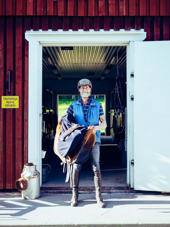 Fredrik Jonsson står i dörren till stallet med en sadel över armen.