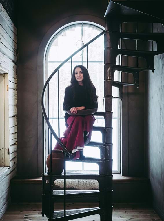Nicole is sitting on the spiral staircase which is located in front of the large window in the hallway.