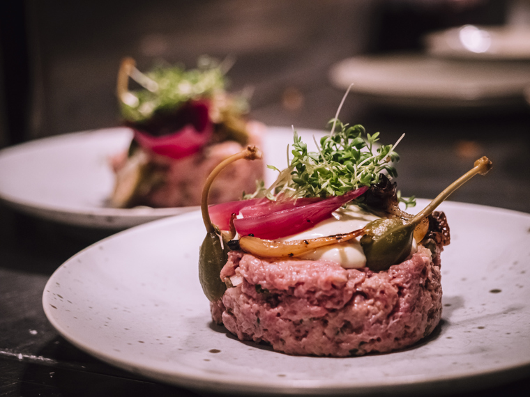 Close-up of two plates with Bryggargatan's steak tartar, topped with capers, pickled onions, and cress.