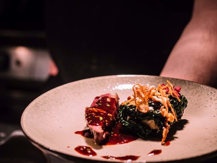 Close up of a plate with wild duck, black cabbage wrapped celeriac, and cherry sauce.