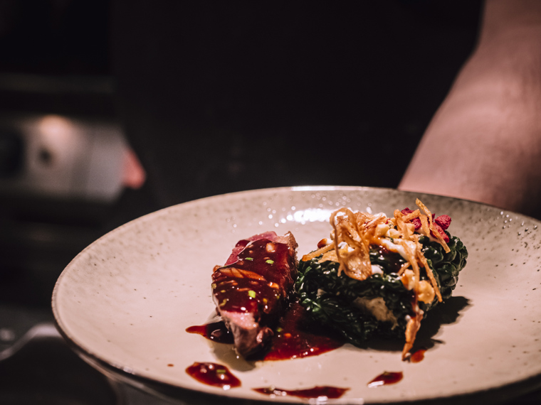 Close up of a plate with wild duck, black cabbage wrapped celeriac, and cherry sauce.