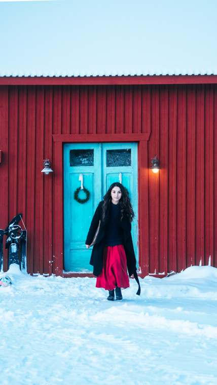 Nicole is walking across the snow-covered ground, coming from the workshop.
