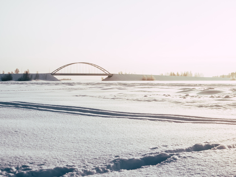 The ice, which is covered with snow, there are some foot and snowmobile tracks. Sundgrundsbron is clearly visible in the background.