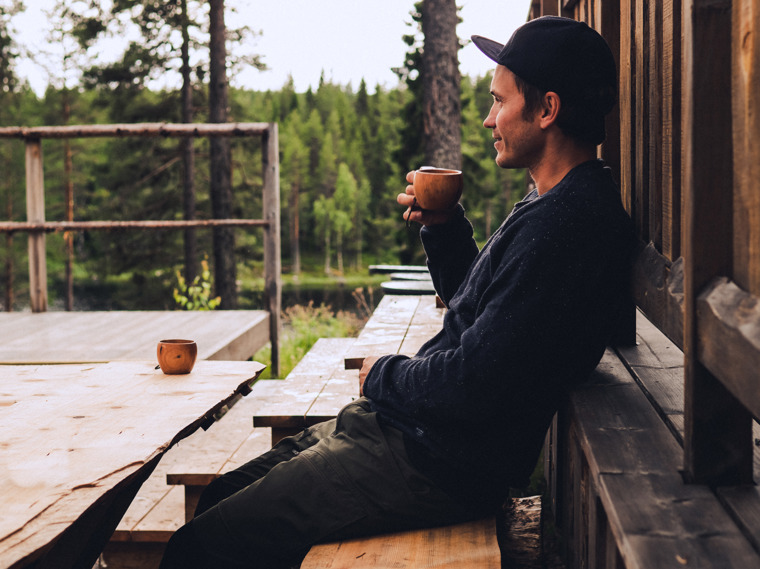 John dricker kaffe ur en träkåsa på en uteplats av trä