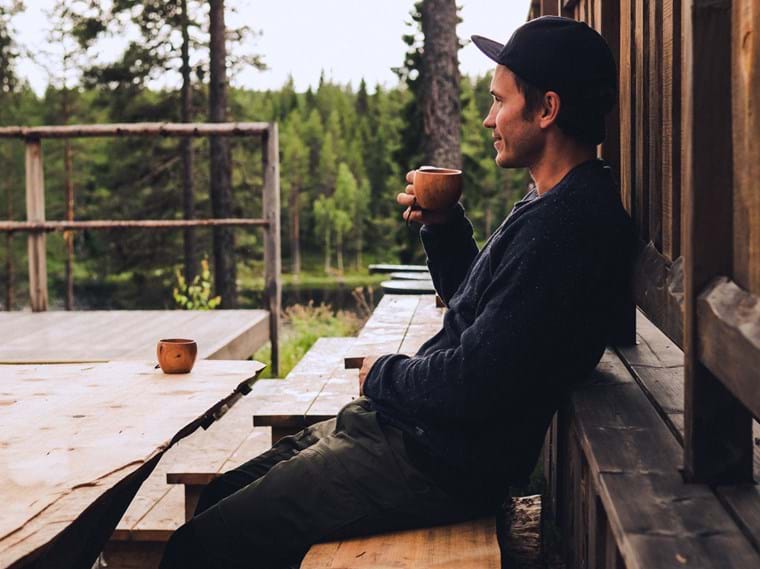 John dricker kaffe ur en träkåsa på en uteplats av trä