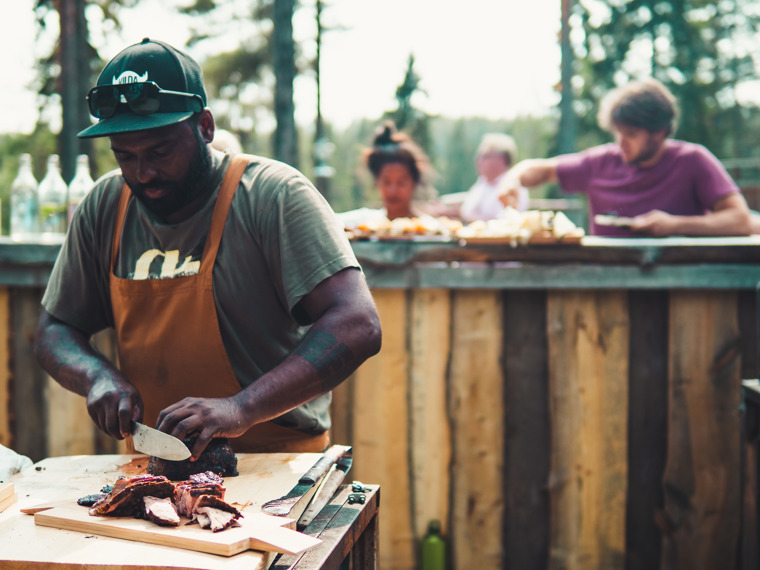 Erik cuts up meat and places it on a wooden plate to be served on the buffet that glimpses in the background.